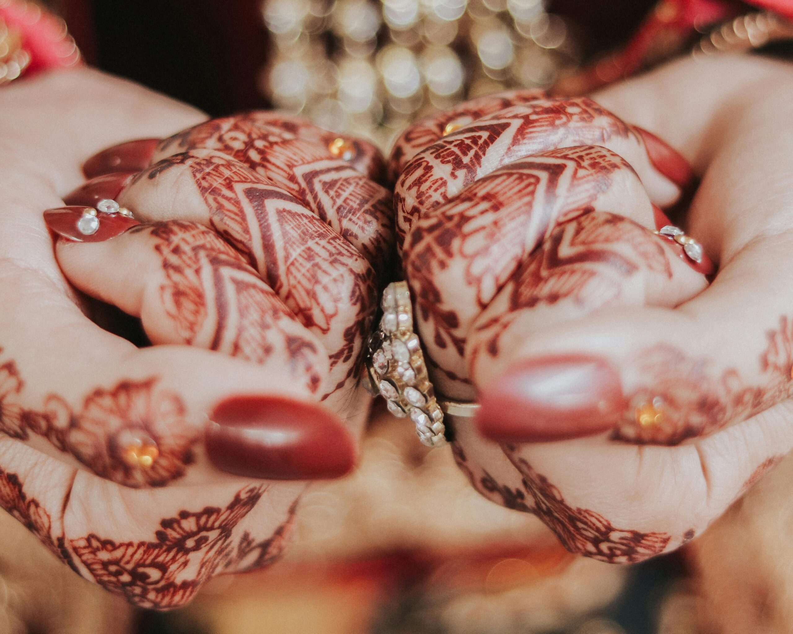 Close-up of detailed bridal henna on hands adorned with jewelry, highlighting cultural elegance.