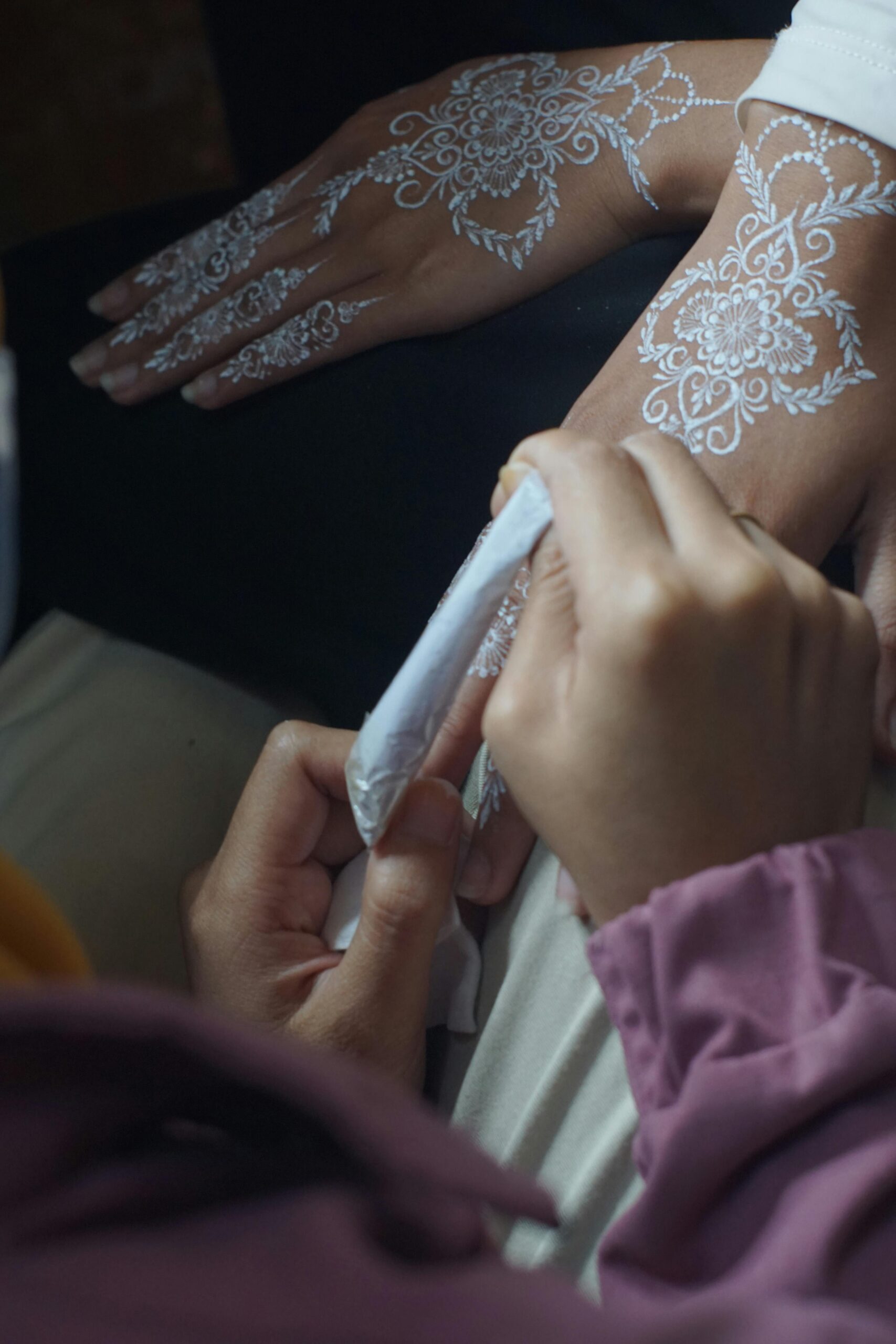 Artist delicately applying white henna to a woman's hand using a fine brush indoors.